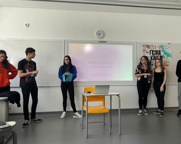 Grupo de 6 alunos, 4 meninas e 2 meninos apresentando uma apresentação de powerpoint sobre a famosa pintora Frida Kahlo