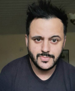 Retrato de Danilo Santos: homem branco de cabelo curto escuro e barba e bigode ralos na mesma cor do cabelo. Rosto afilado, nariz fino, testa larga, lábios grossos e boca pequena. Usando uma camiseta preta, em uma fotografia tirada do pescoço para cima, ele posa sério, sem esboçar qualquer sorriso, e com a sobrancelha esquerda saltada. Ele se mostra um pouco inclinado para esquerda. No fundo, tanto a parede quanto o teto do ambiente são vistos, os dois lisos.