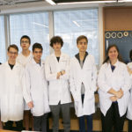 Grupo de alunos com jaleco branco e coma professora doutora bióloga Luciana Vasques na sala STEAM do Colégio Miguel de Cervantes